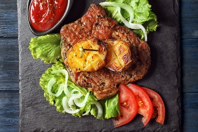 Photo of Slate plate with tasty grilled meat, potatoes and sauce on table, top view