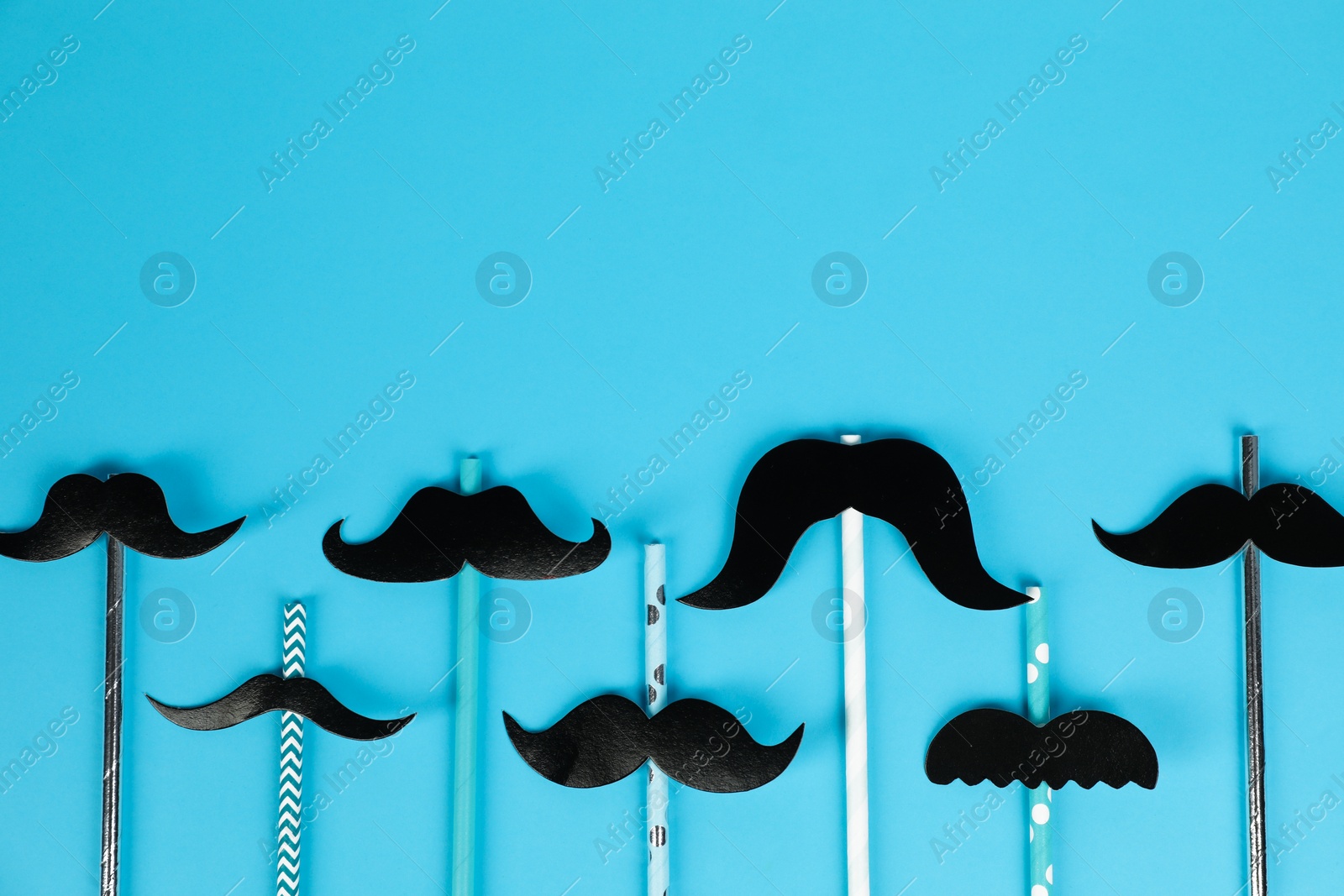 Photo of Fake paper mustaches with party props on light blue background, flat lay. Space for text