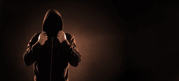 Image of Anonymous man in hood on black background, space for text. Banner design, color toned