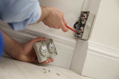 Photo of Electrician with screwdriver repairing power socket indoors, closeup