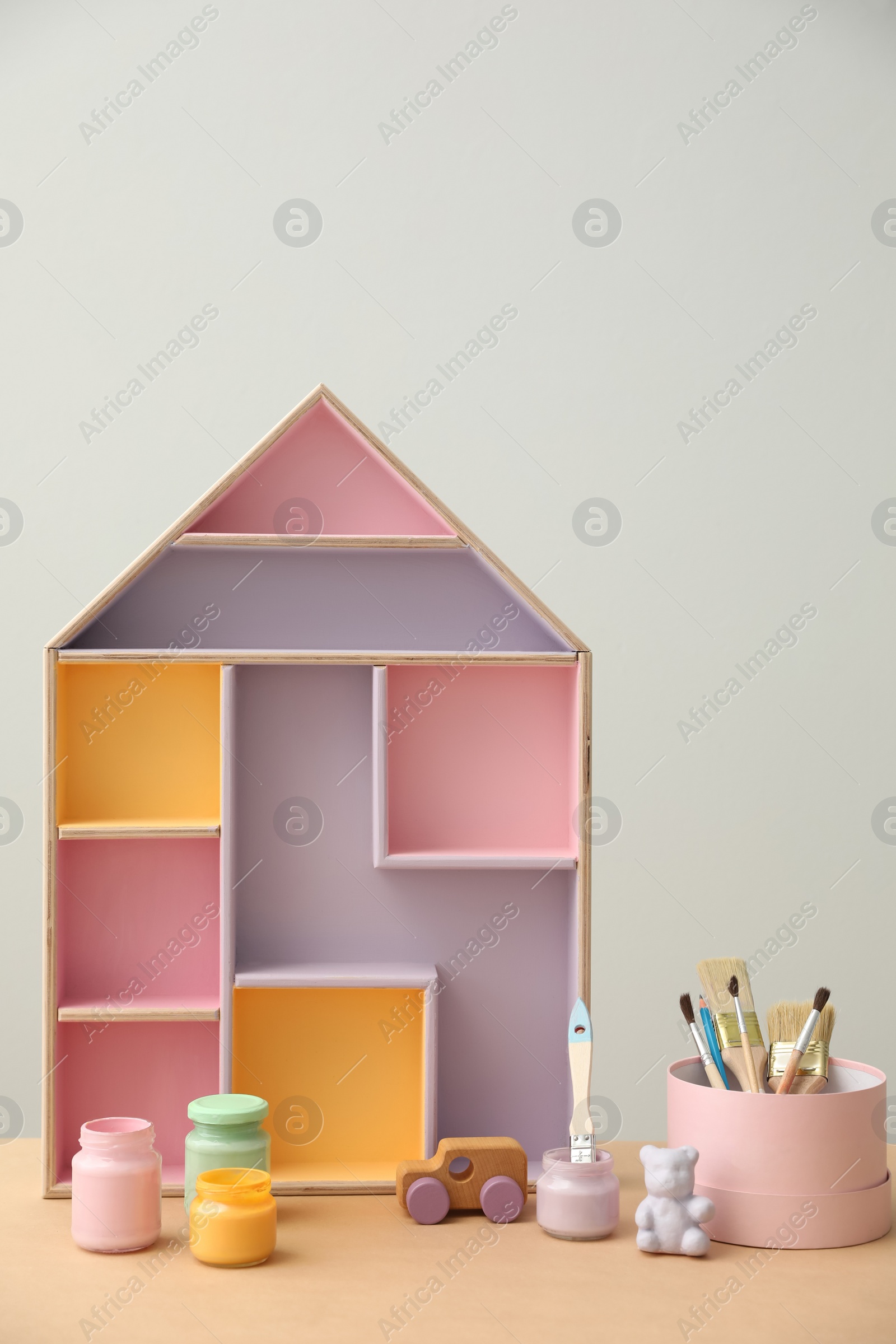 Photo of Composition with house shaped shelf and jars of paints on table. Interior element