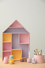 Photo of Composition with house shaped shelf and jars of paints on table. Interior element