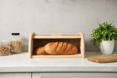 Wooden bread basket with freshly baked loaves on white marble table in kitchen