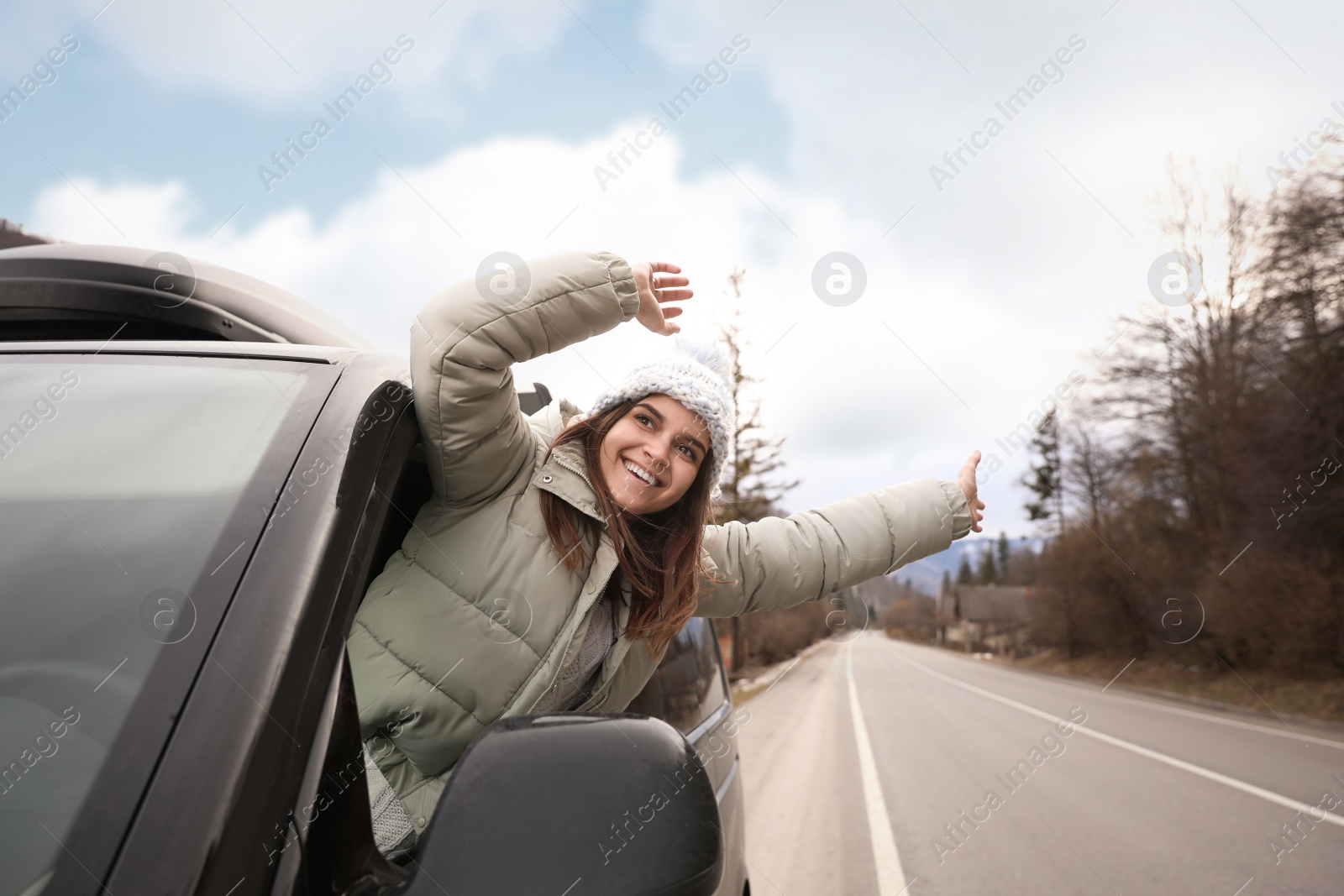 Photo of Happy woman leaning out of car window on road. Winter vacation