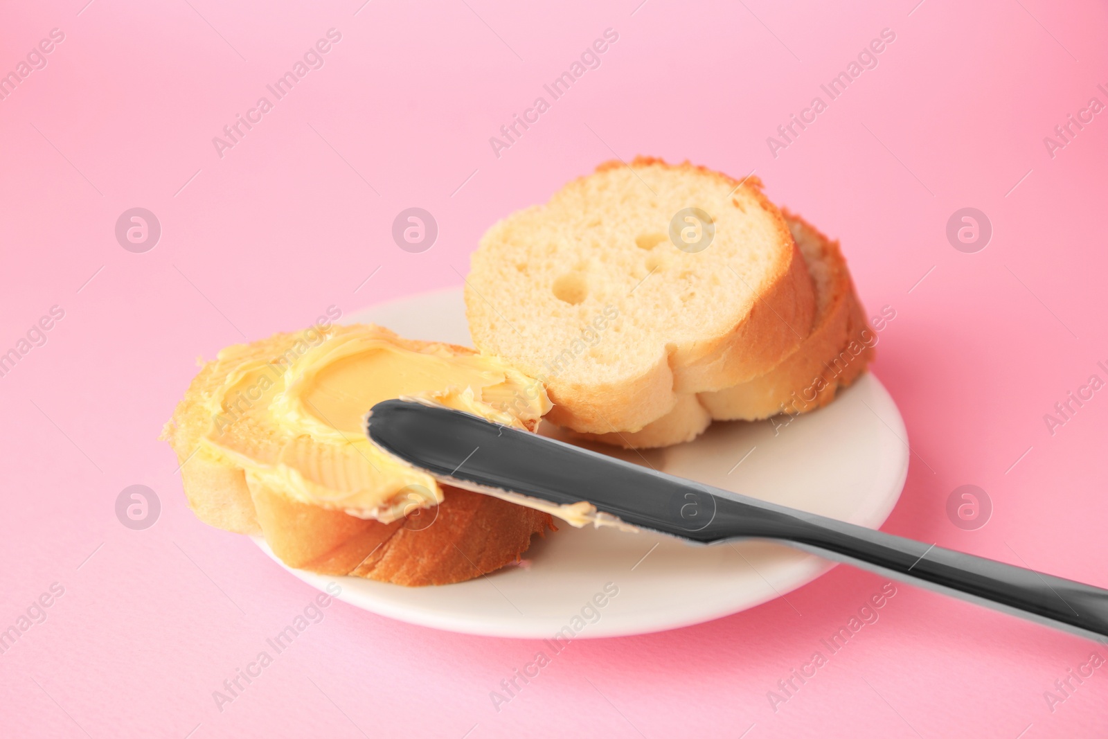 Photo of Slices of delicious baguette with butter and knife on pale pink background