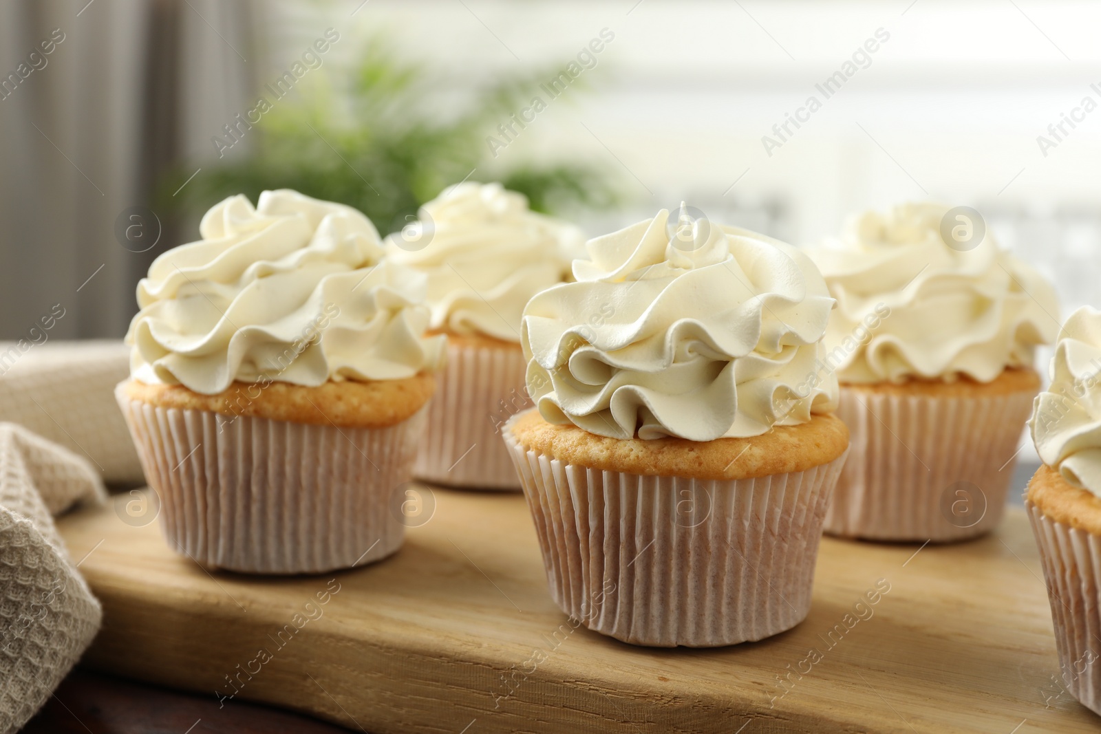 Photo of Tasty cupcakes with vanilla cream on wooden table, closeup