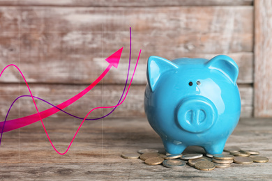 Image of Blue piggy bank with coins and graph on wooden background