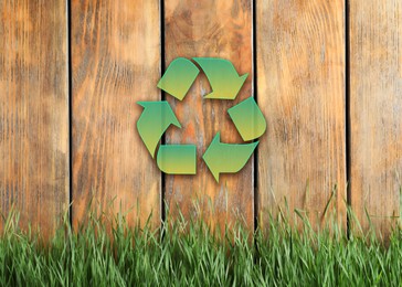 Green grass and illustration of recycling symbol on wooden fence