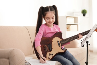 Photo of Little girl with guitar writing music notes at home