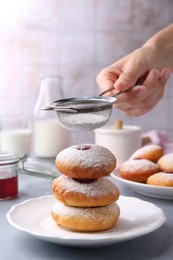 Woman dusting powdered sugar onto delicious Hanukkah donuts on light grey table, closeup