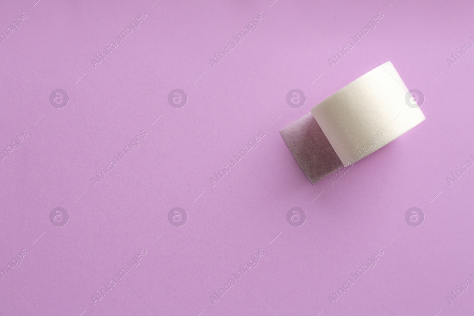 Photo of Sticking plaster roll on lilac background, top view. Space for text