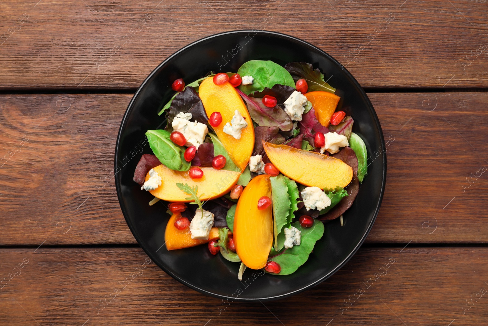 Photo of Delicious persimmon salad with pomegranate and spinach on wooden table, top view