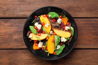 Delicious persimmon salad with pomegranate and spinach on wooden table, top view