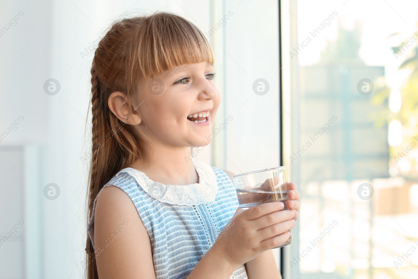 Photo of Cute little girl holding glass of fresh water at home