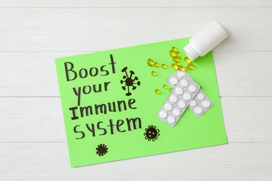 Paper sheet with text Boost your Immune System and different pills on white wooden table, top view