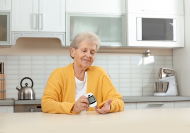 Photo of Senior woman using digital glucometer at home. Diabetes control