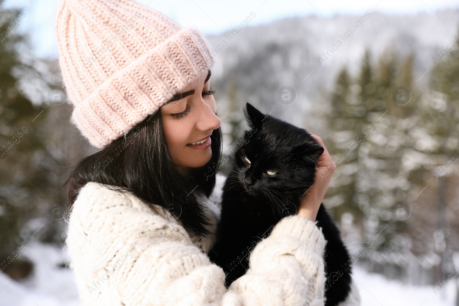 Photo of Happy young woman with black cat outdoors on winter day