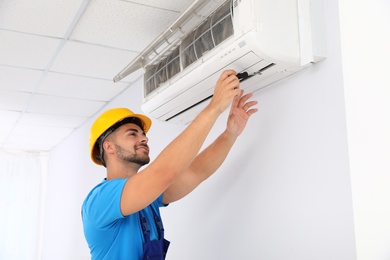 Photo of Professional technician maintaining modern air conditioner indoors