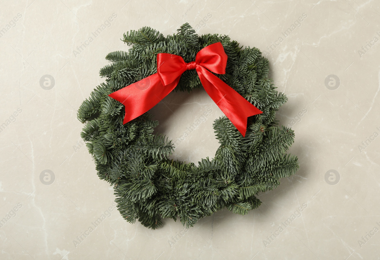 Photo of Christmas wreath made of fir tree branches with red ribbon on light grey marble background