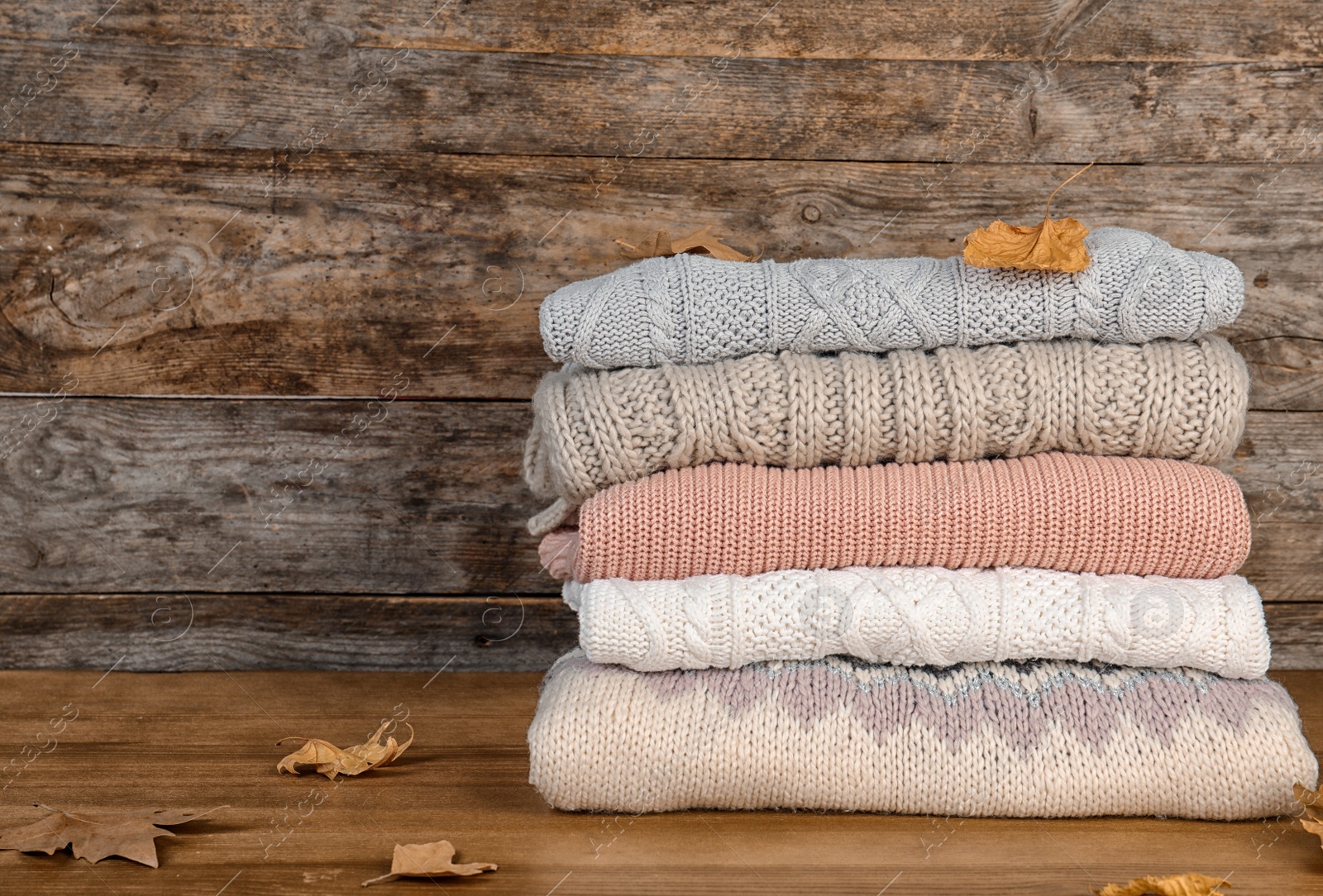 Photo of Stack of warm clothes and autumn leaves on wooden table. Space for text