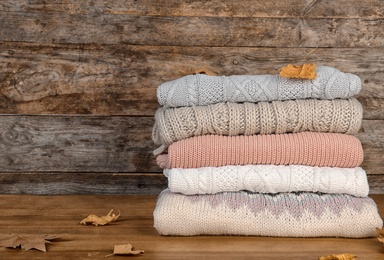 Photo of Stack of warm clothes and autumn leaves on wooden table. Space for text