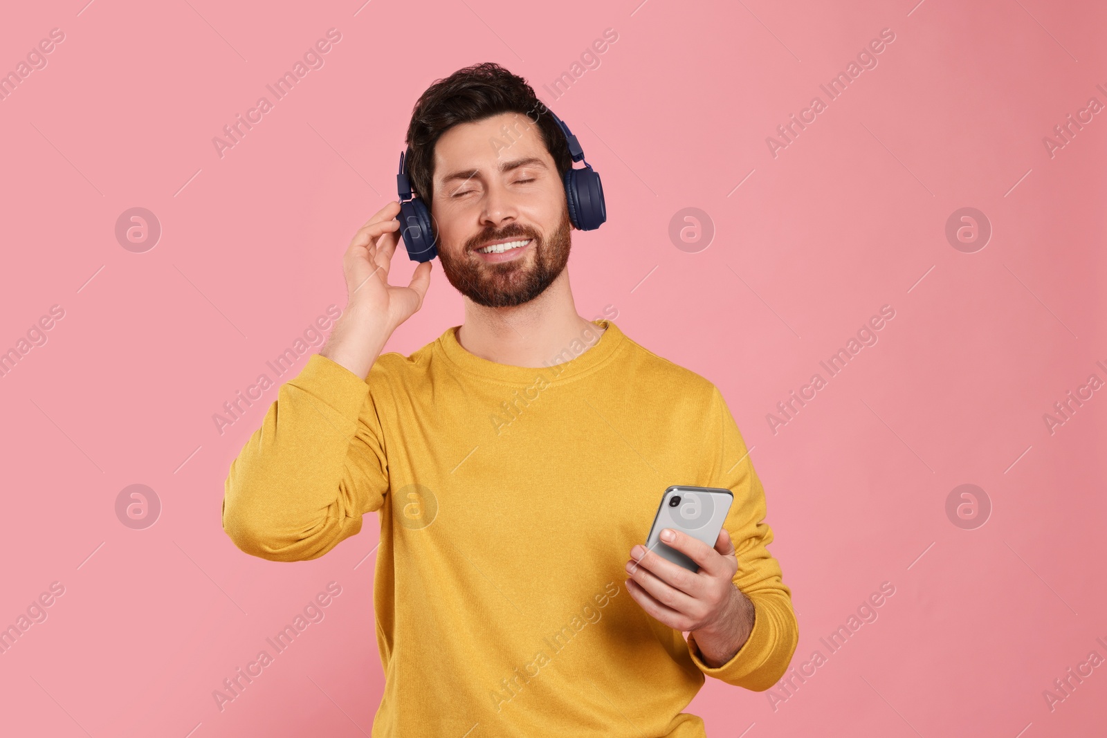 Photo of Happy man listening music with headphones on pink background