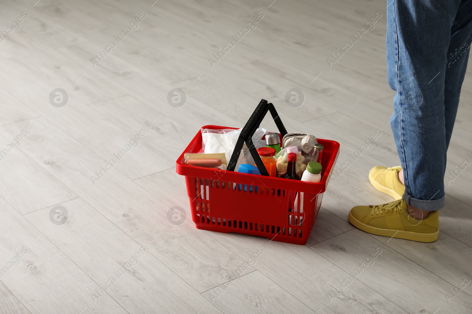 Photo of Woman and shopping basket with groceries on white wooden floor, closeup