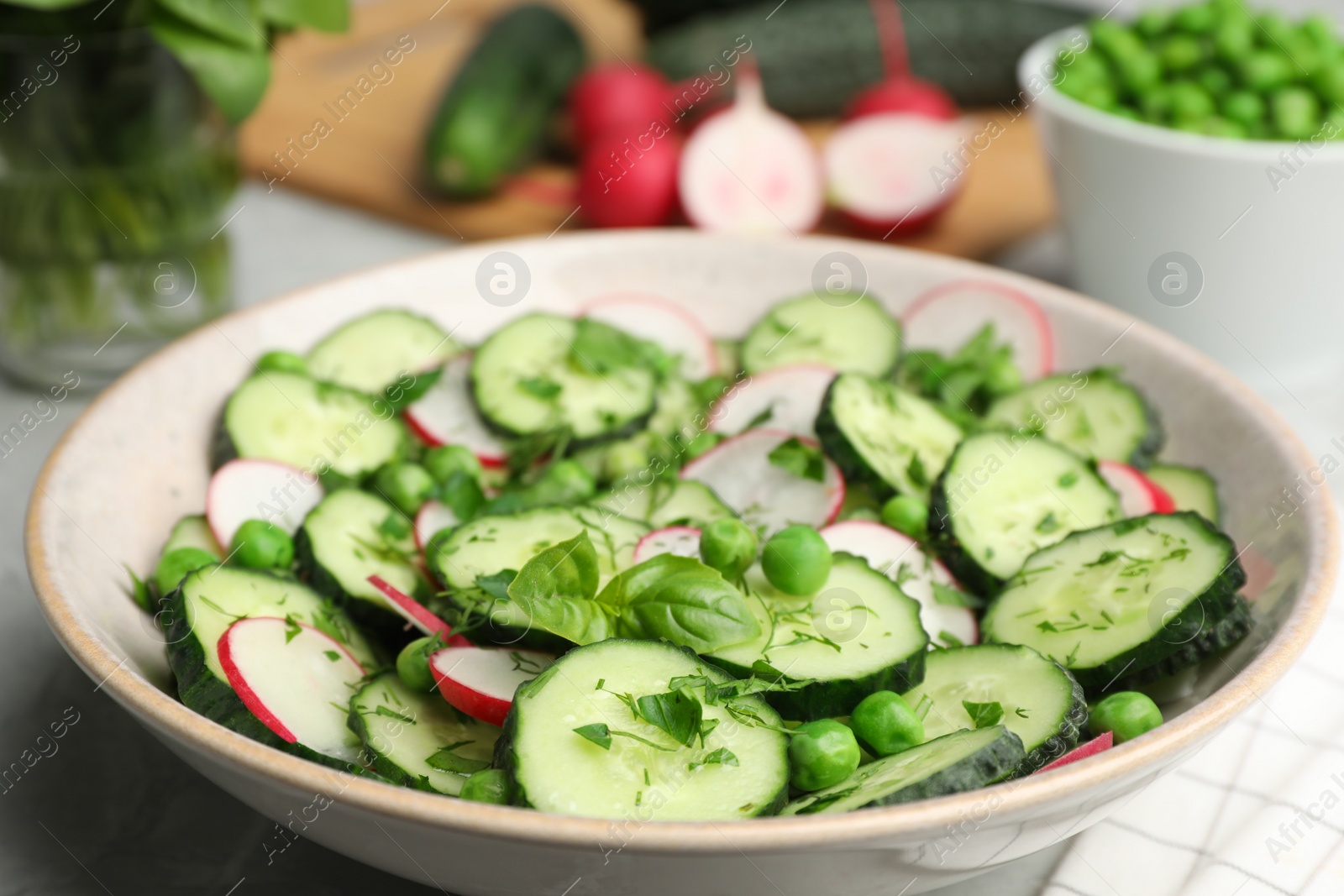 Photo of Appetizing salad with cucumbers, radish and pea in bowl on table, closeup