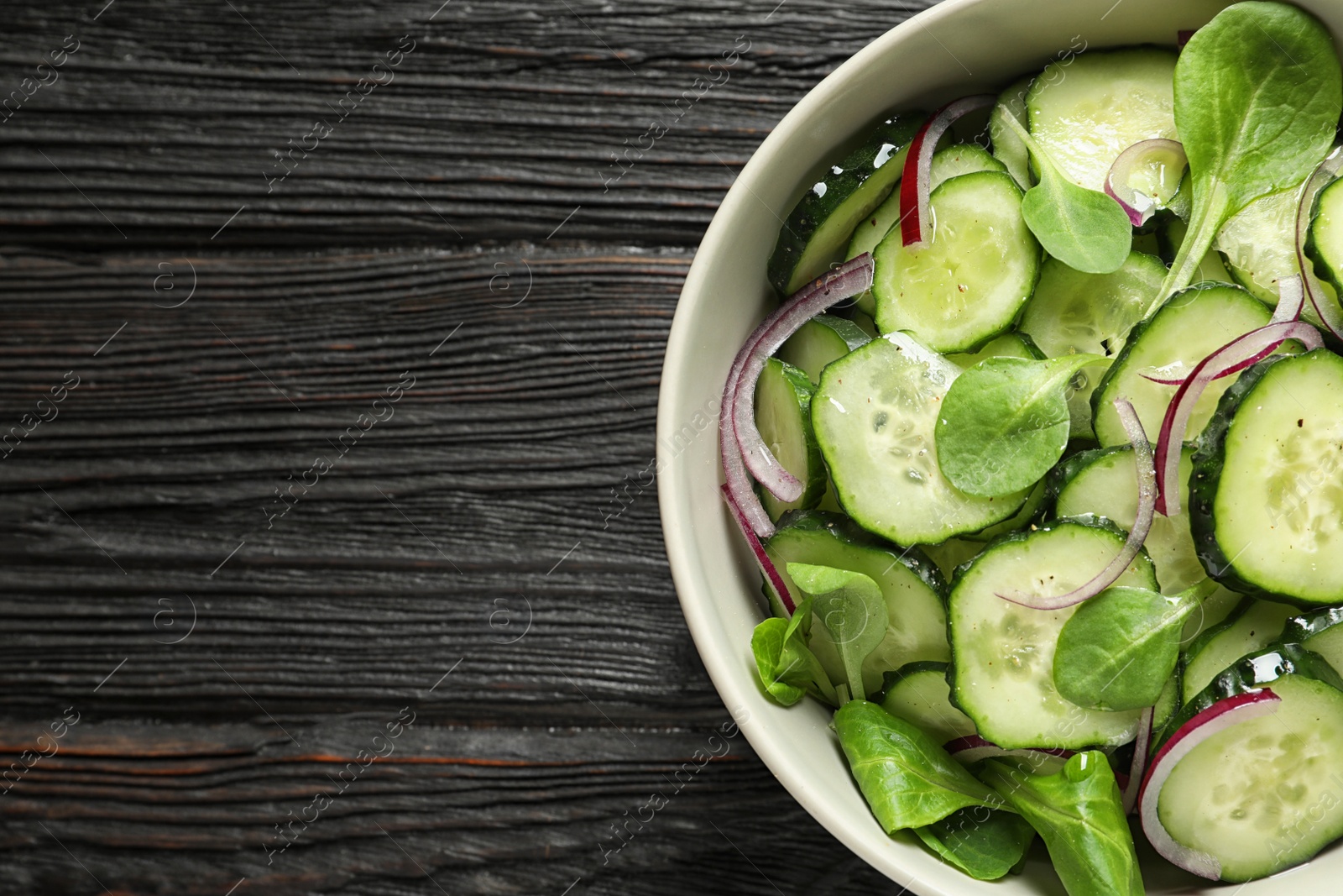 Photo of Delicious cucumber salad with onion and spinach in bowl on wooden background, top view. Space for text