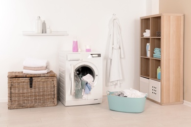 Photo of Washing machine with dirty clothes and towels in laundry room