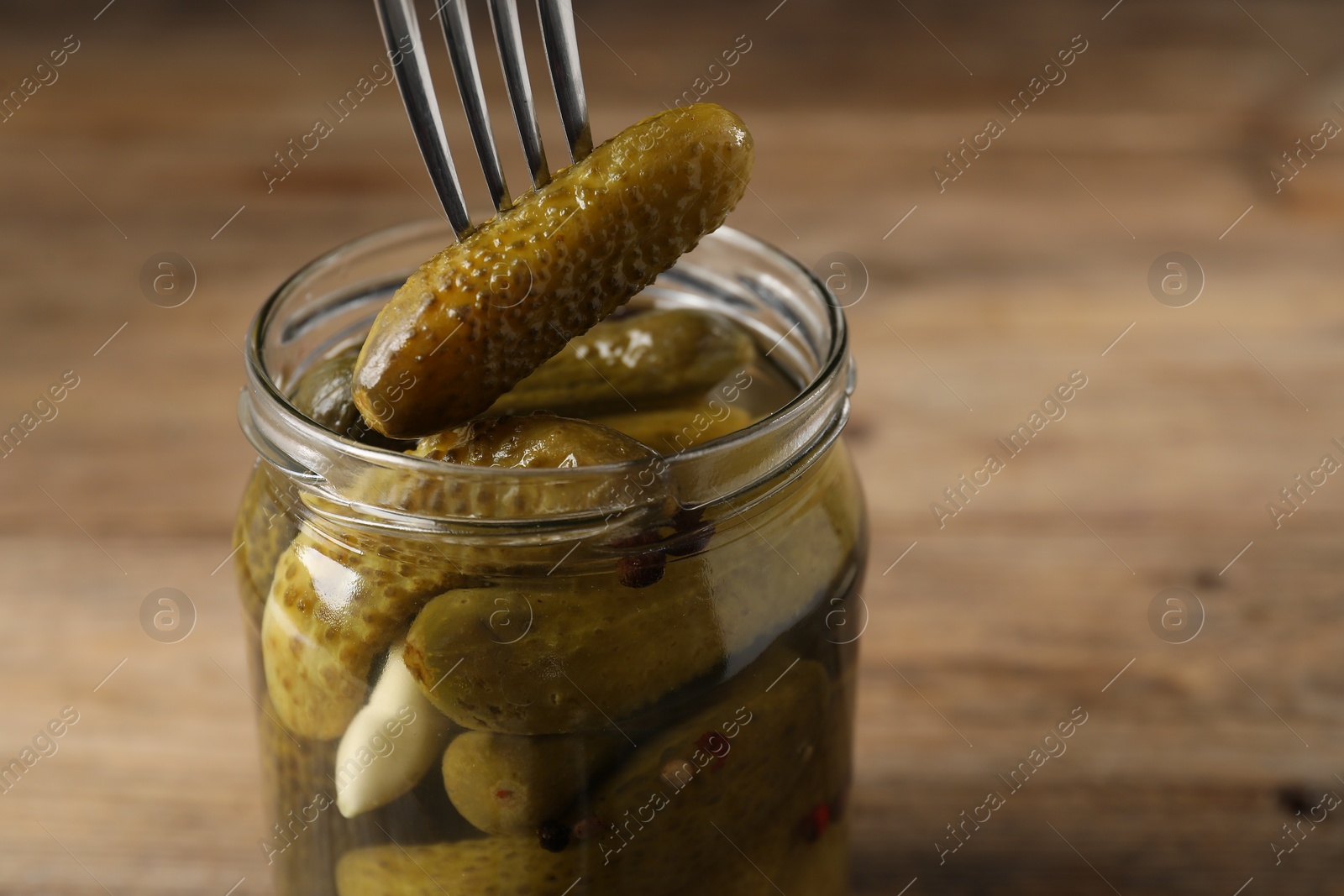 Photo of Eating tasty pickled cucumber from jar at table, closeup