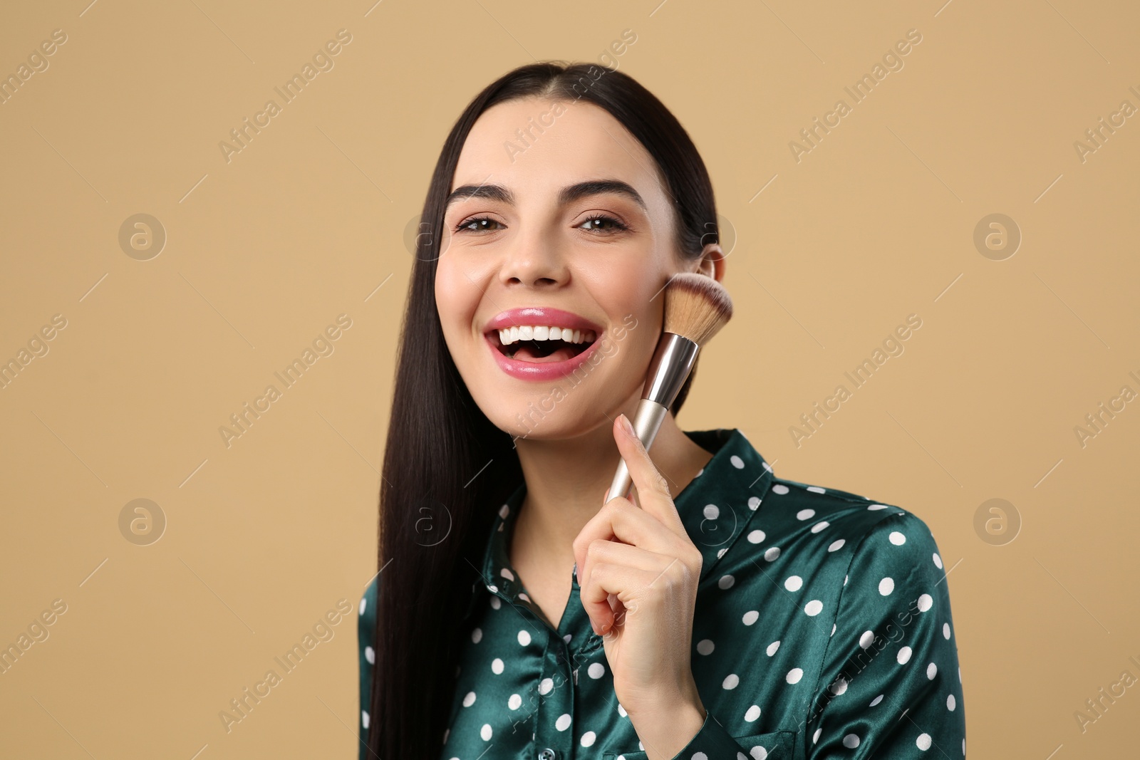 Photo of Happy woman with makeup brush on light brown background