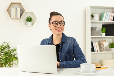 Photo of Home workplace. Happy woman near laptop at white desk in room