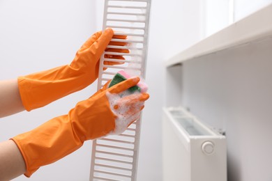 Woman washing radiator grill with sponge and detergent indoors, closeup