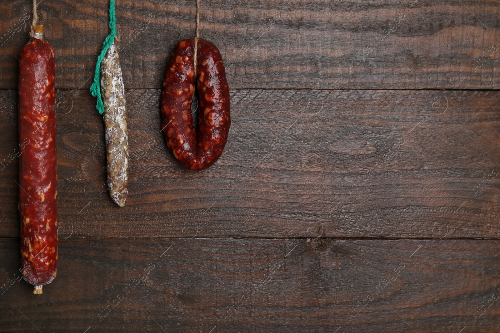 Photo of Different delicious sausages hanging near wooden wall. Space for text