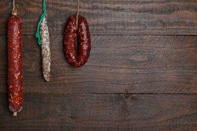 Different delicious sausages hanging near wooden wall. Space for text