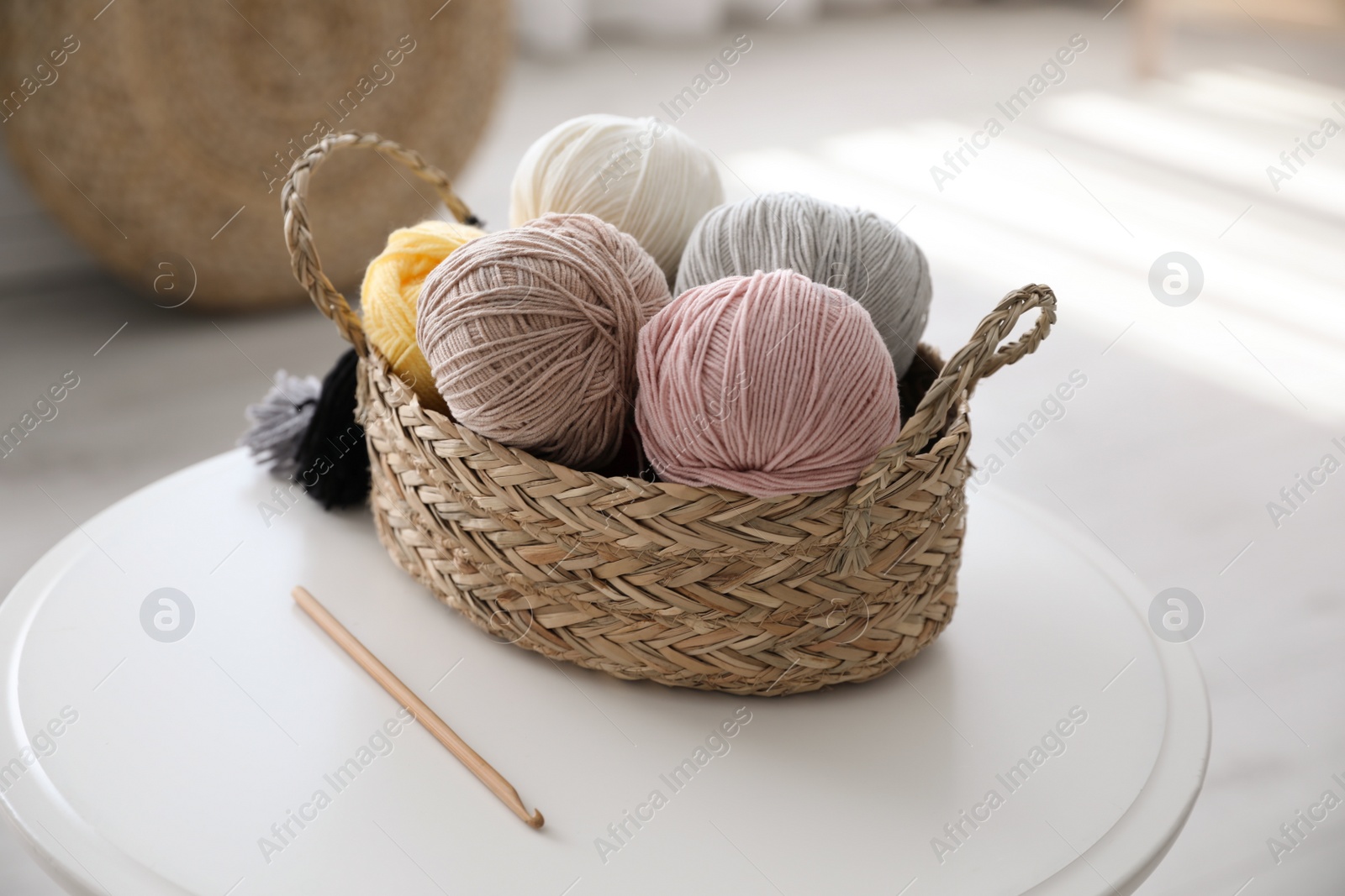 Photo of Wicker basket with clews and crochet on table indoors. Engaging in hobby