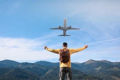 Man looking at airplane flying in sky over mountains, back view