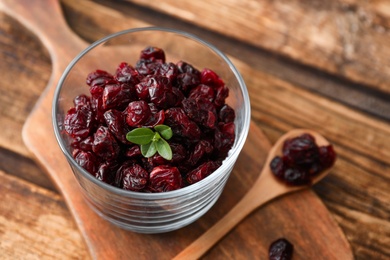 Photo of Tasty dried cranberries and leaves in glass on wooden table, closeup