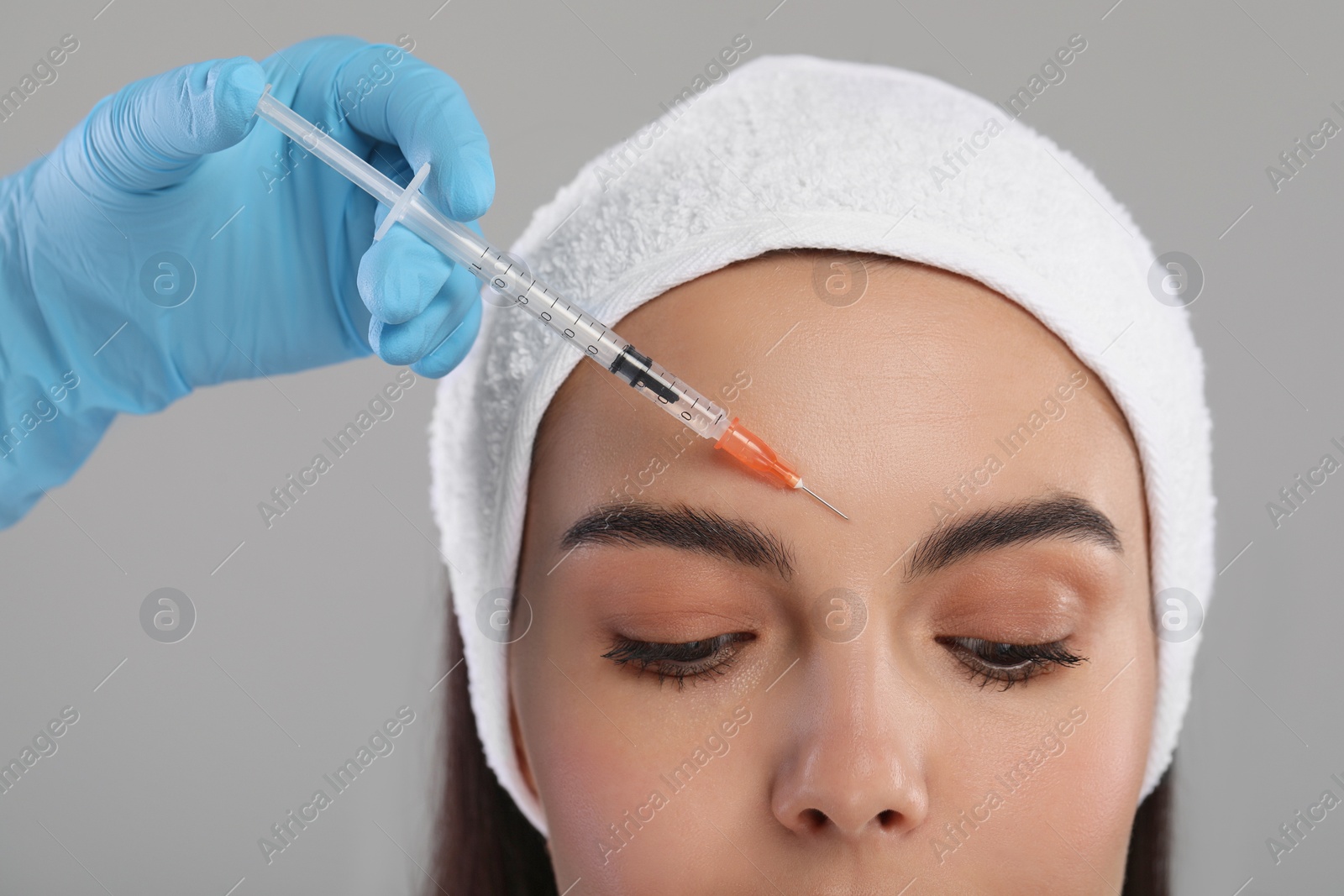 Photo of Doctor giving facial injection to young woman on light grey background, closeup. Cosmetic surgery