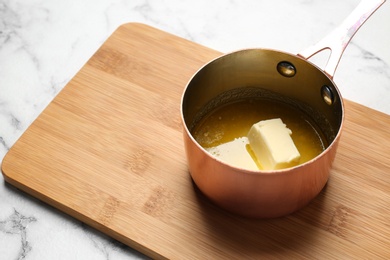 Saucepan with melting butter on wooden board. Space for text