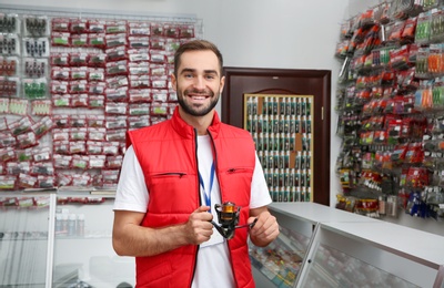 Salesman with spinning reel in sports shop. Fishing equipment