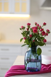 Photo of Glass vase with fresh flowers and towel on table in kitchen