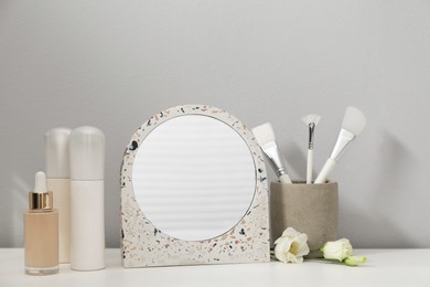 Photo of Stylish round mirror and cosmetic products on dressing table near white wall
