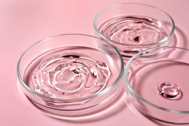 Petri dishes with liquids on pale pink background, closeup