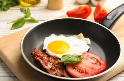 Photo of Pan with fried sunny side up egg, bacon and tomato on table