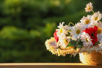 Photo of Beautiful wild flowers in wicker basket on wooden table against blurred background, space for text
