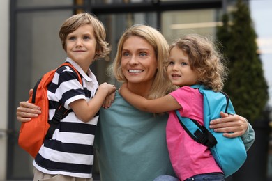 Photo of Happy woman hugging with her children near kindergarten outdoors