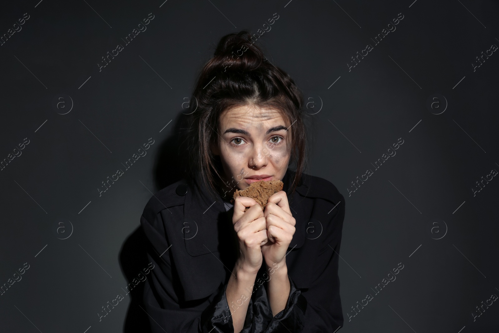 Photo of Poor woman with piece of bread on dark background