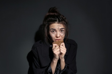 Poor woman with piece of bread on dark background